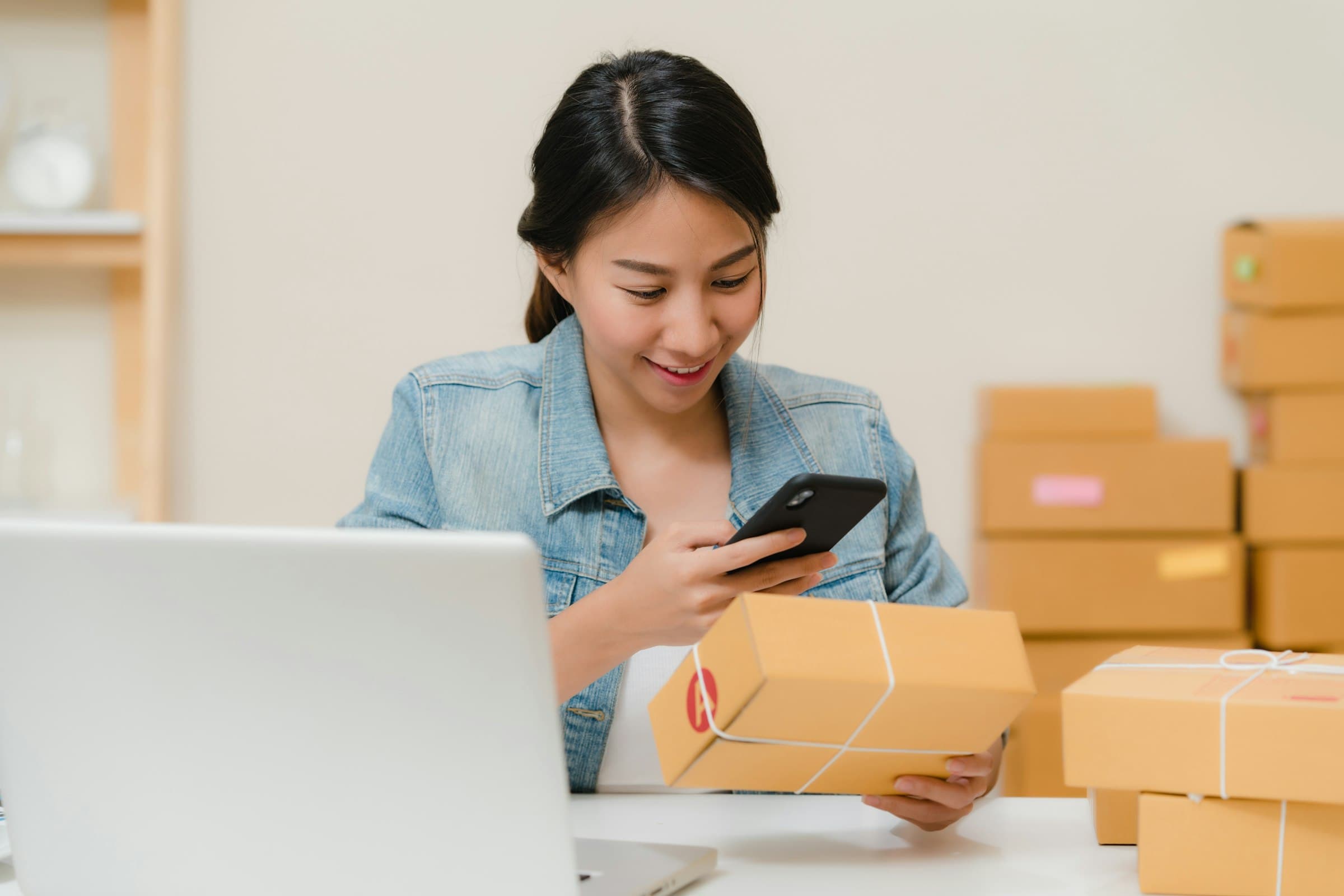 A merchant checking a shipping label on a package while working from a laptop