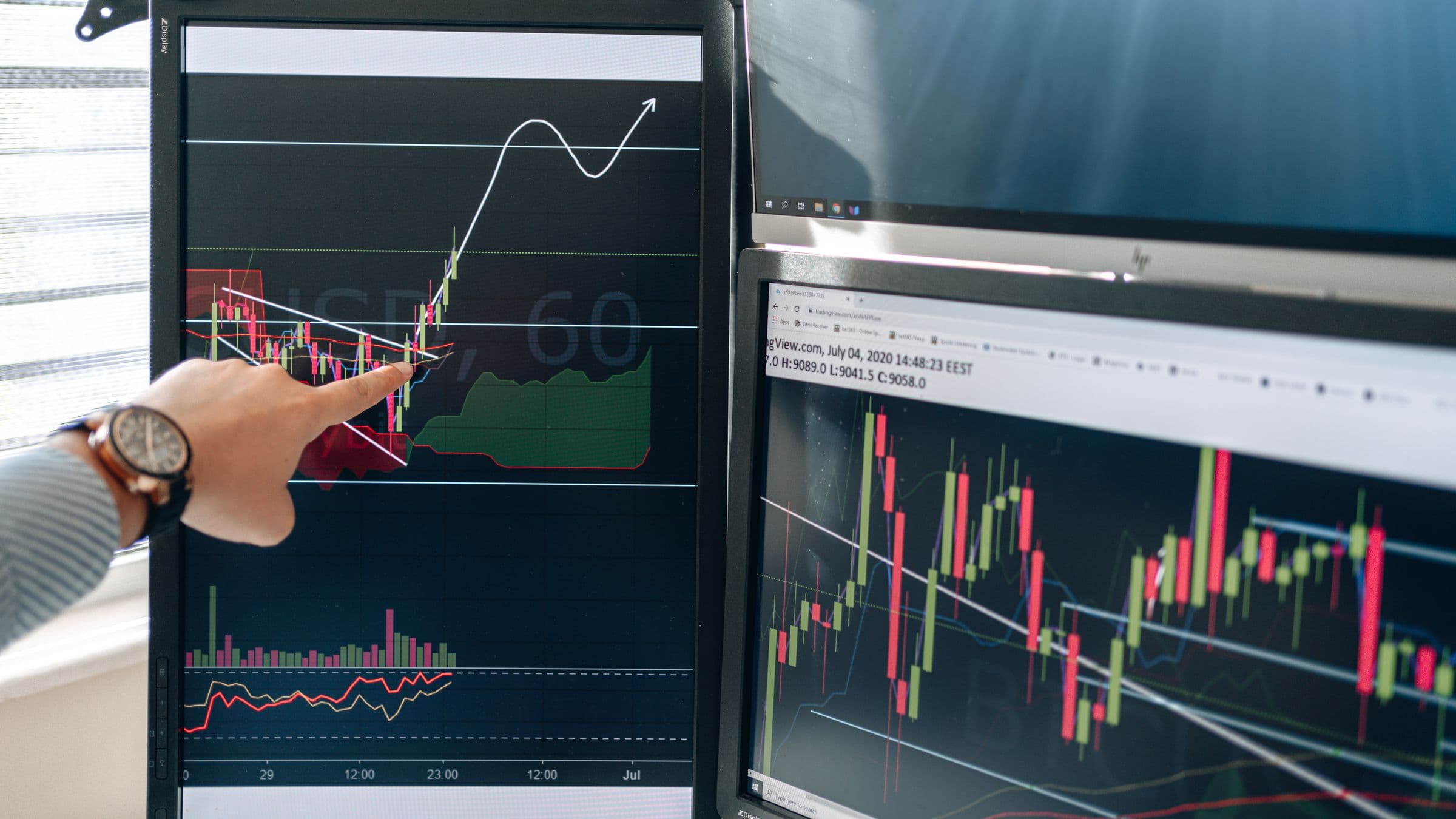 A team member pointing at trading and analytics dashboards across multiple monitors
