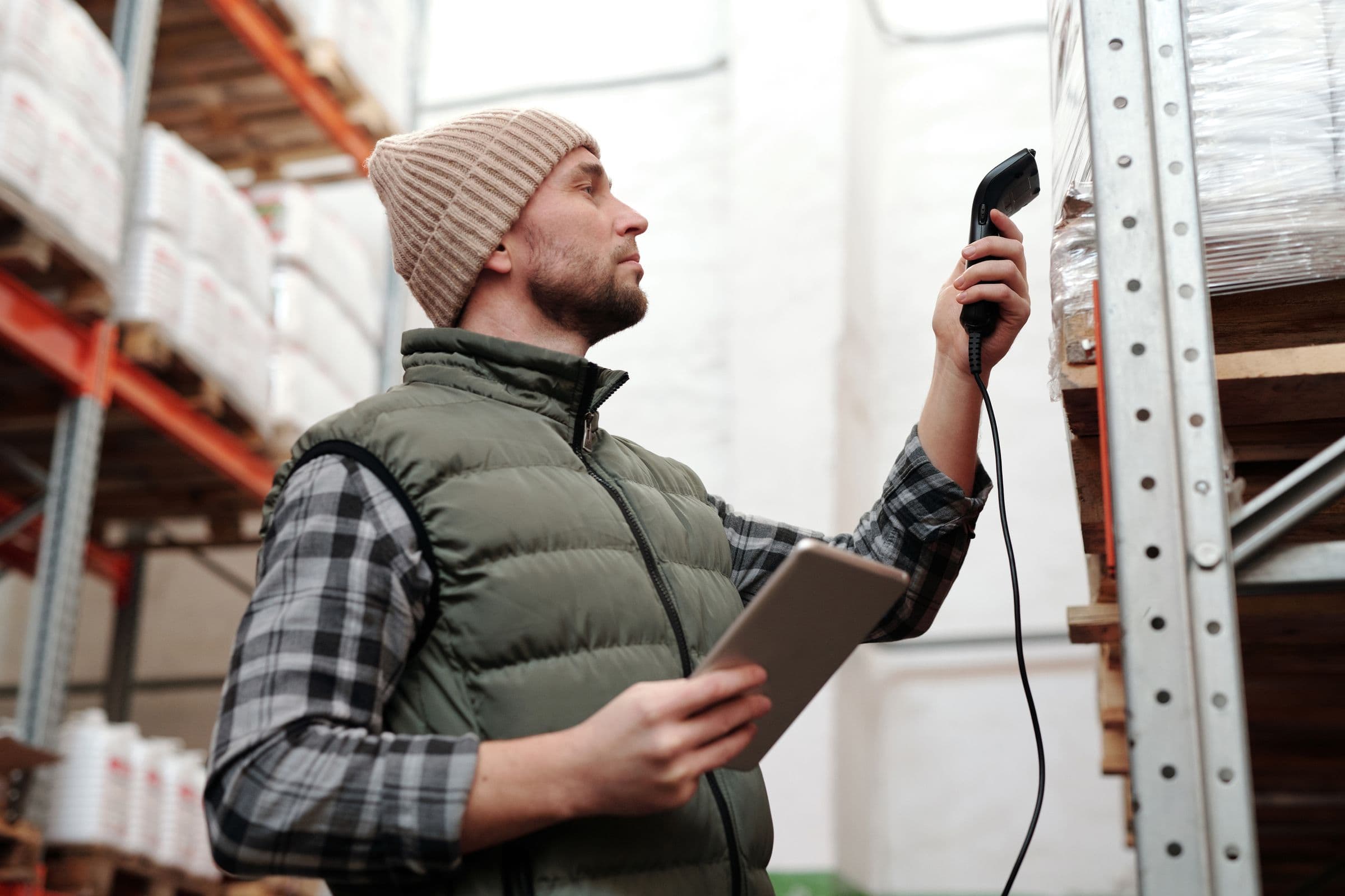 A warehouse worker checking stock with a handheld scanner and tablet while planning inventory